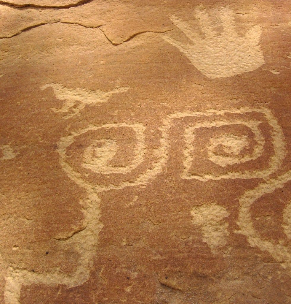 Petroglyphen der Ancestral Pueblo mit einem Handabdruck, einem Vogel und Spiralmustern, eingeritzt in eine Sandsteinfelswand im Mesa-Verde-Nationalpark.